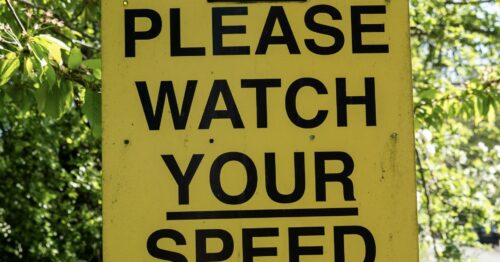 A yellow traffic sign mounted on a post that reads "Please Watch Your Speed", with a speed indicator icon at the top.